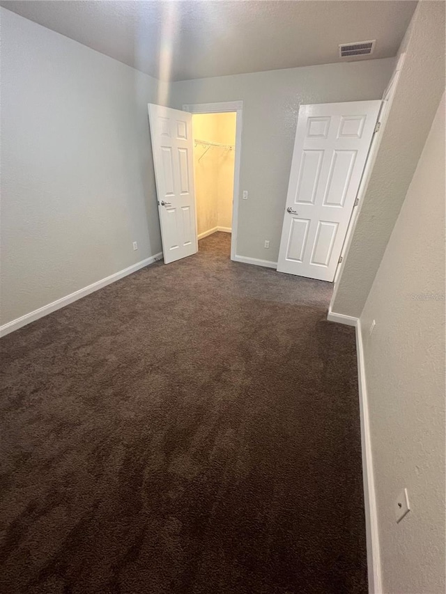 unfurnished bedroom featuring a walk in closet and dark carpet