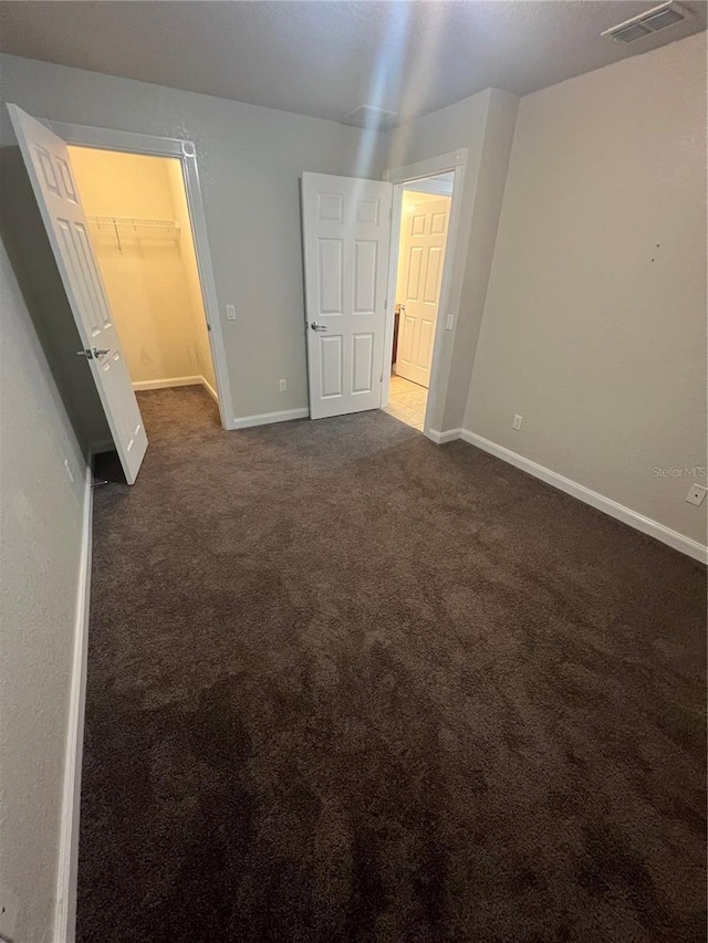 unfurnished bedroom featuring a walk in closet and dark colored carpet