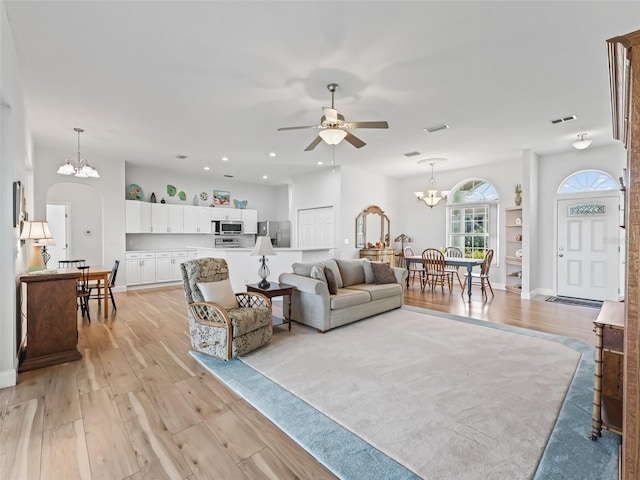 living room featuring arched walkways, visible vents, ceiling fan with notable chandelier, and light wood-style floors