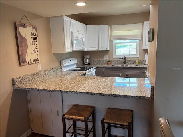 1152 Villa Ln Unit 104, Apopka, FL 32712 - kitchen with sink, white appliances, a breakfast bar area, white cabinets, and kitchen peninsula