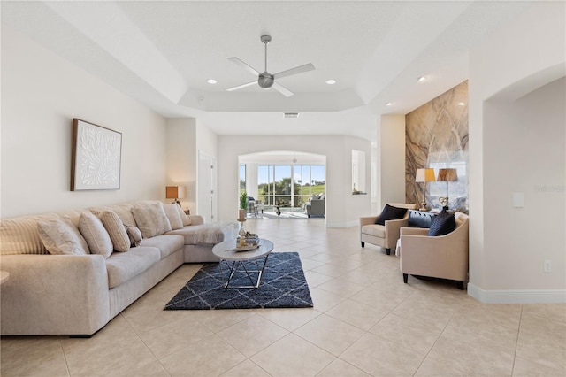 tiled living room with ceiling fan and a tray ceiling