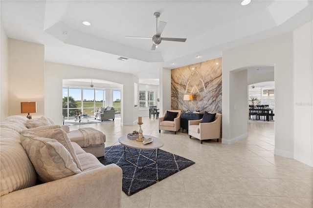 living room with light tile patterned floors, a raised ceiling, and ceiling fan