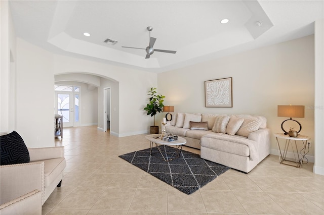 living room featuring light tile patterned flooring, ceiling fan, and a raised ceiling