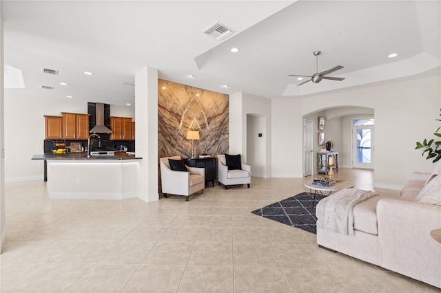 tiled living room with sink, a raised ceiling, and ceiling fan