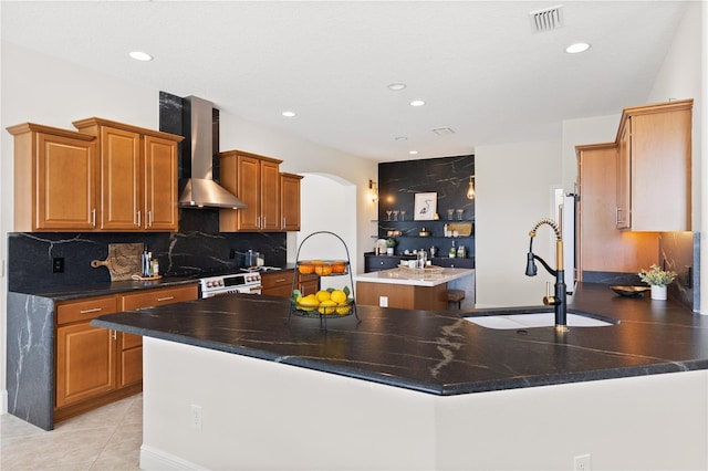 kitchen with wall chimney exhaust hood, sink, a center island with sink, kitchen peninsula, and backsplash