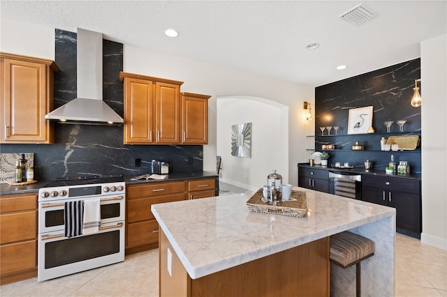 kitchen with beverage cooler, double oven range, a center island, light stone countertops, and wall chimney exhaust hood