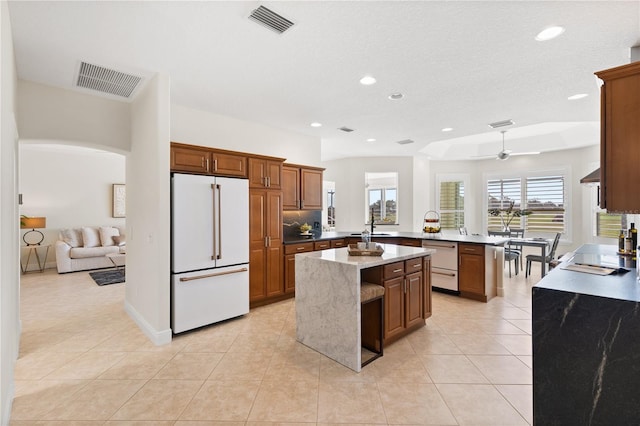 kitchen with light tile patterned floors, white appliances, ceiling fan, a kitchen island, and kitchen peninsula