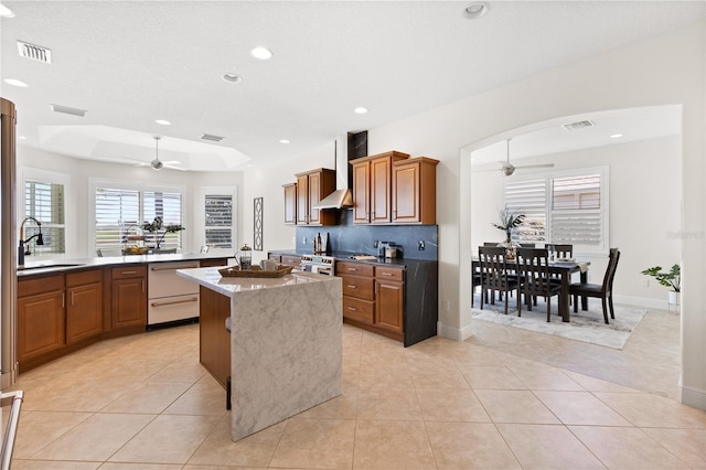 kitchen with sink, light tile patterned floors, a kitchen island, ceiling fan, and wall chimney range hood