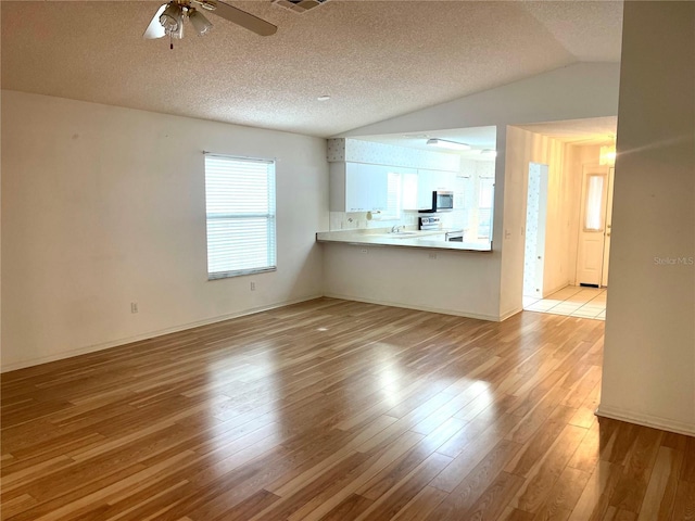 unfurnished living room with ceiling fan, light wood-style flooring, a textured ceiling, vaulted ceiling, and a sink