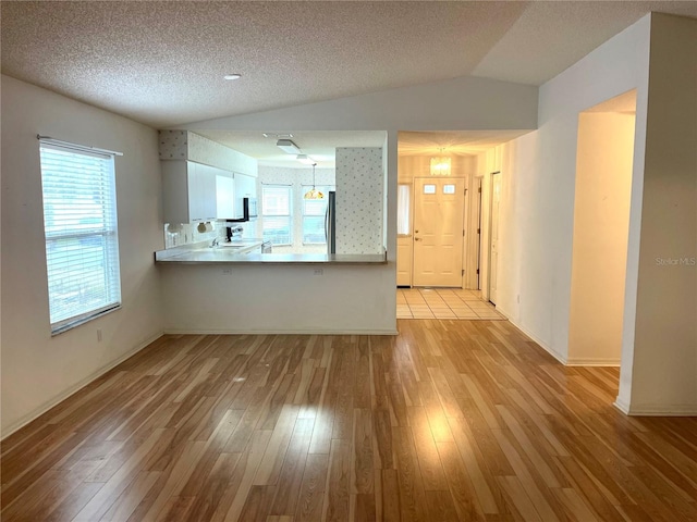 unfurnished living room with a wealth of natural light, light wood finished floors, and vaulted ceiling