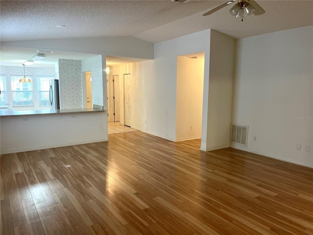 unfurnished living room with visible vents, a ceiling fan, wood finished floors, and lofted ceiling