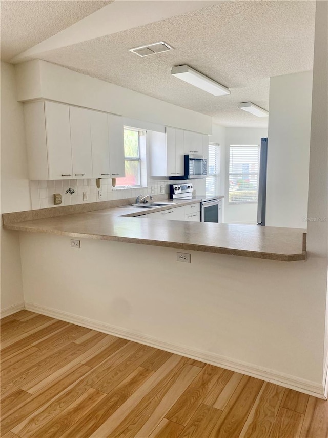 kitchen with a peninsula, light wood-style floors, visible vents, and appliances with stainless steel finishes
