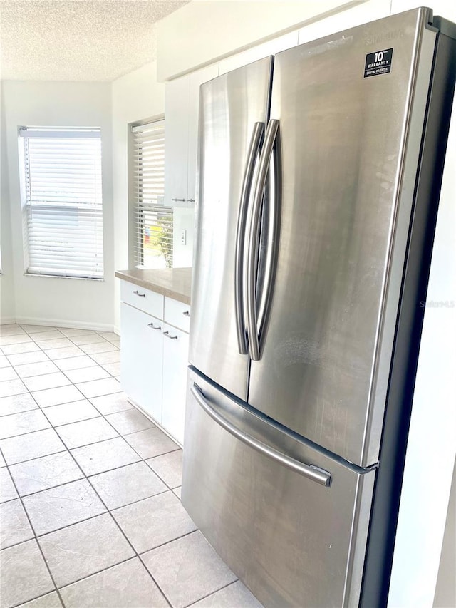 kitchen with light countertops, a textured ceiling, freestanding refrigerator, light tile patterned flooring, and white cabinets
