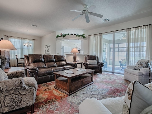 living room with ceiling fan with notable chandelier, a wealth of natural light, and a textured ceiling