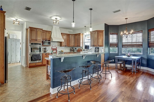 kitchen featuring a breakfast bar area, light stone counters, decorative light fixtures, custom range hood, and stainless steel appliances