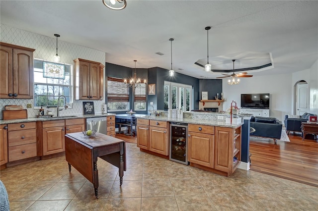 kitchen with sink, an island with sink, decorative light fixtures, stainless steel dishwasher, and beverage cooler