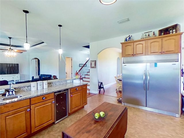 kitchen featuring decorative light fixtures, stainless steel built in refrigerator, sink, wine cooler, and light stone counters