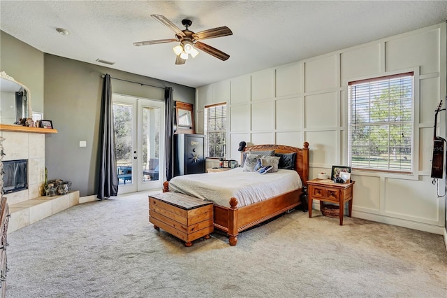 carpeted bedroom with a tile fireplace, ceiling fan, a textured ceiling, access to outside, and french doors