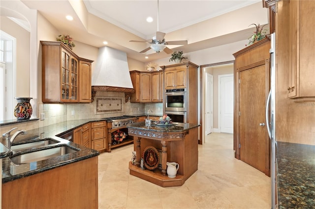 kitchen with sink, appliances with stainless steel finishes, tasteful backsplash, custom range hood, and an island with sink