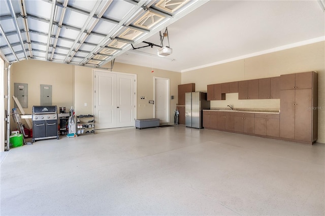 garage with a garage door opener, sink, electric panel, and stainless steel refrigerator