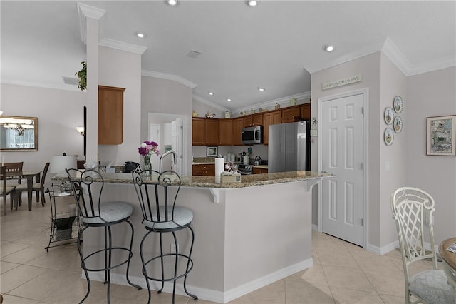 kitchen with a breakfast bar, stainless steel appliances, dark stone counters, and ornamental molding