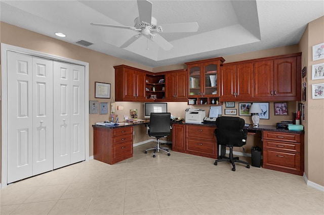 office featuring light tile patterned flooring, ceiling fan, built in desk, and a raised ceiling