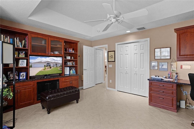 office featuring a tray ceiling, ceiling fan, light tile patterned floors, and a textured ceiling