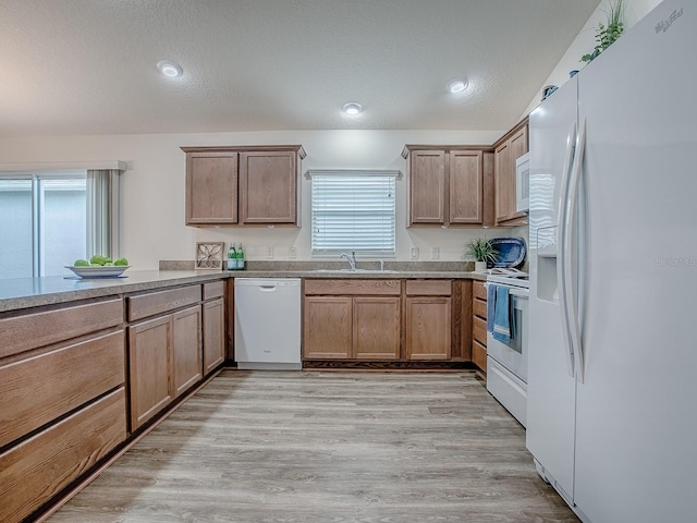 kitchen with light wood-type flooring, sink, a textured ceiling, and white appliances