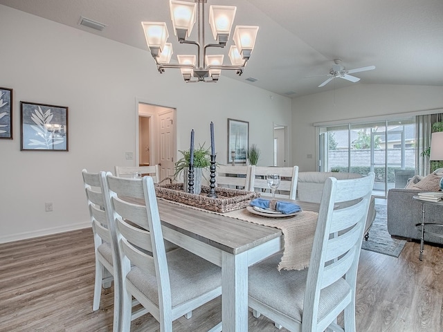 dining room with ceiling fan with notable chandelier, vaulted ceiling, and light wood-type flooring