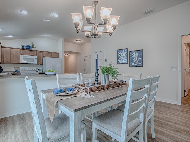 dining space featuring vaulted ceiling, an inviting chandelier, and light hardwood / wood-style floors