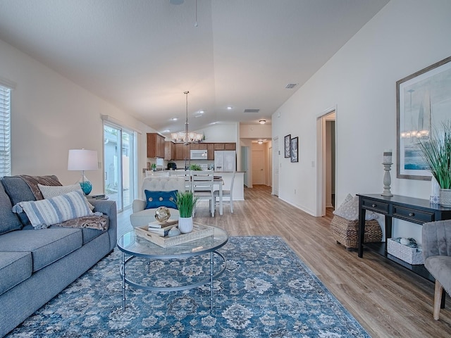 living room with lofted ceiling, a notable chandelier, and light hardwood / wood-style floors