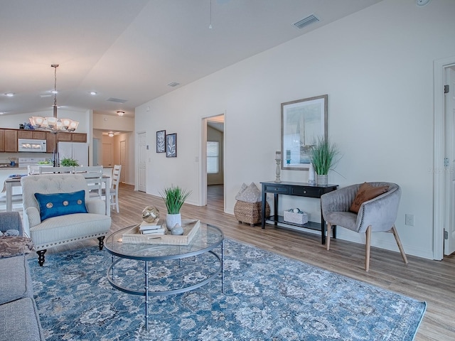 living room featuring vaulted ceiling, an inviting chandelier, and light wood-type flooring