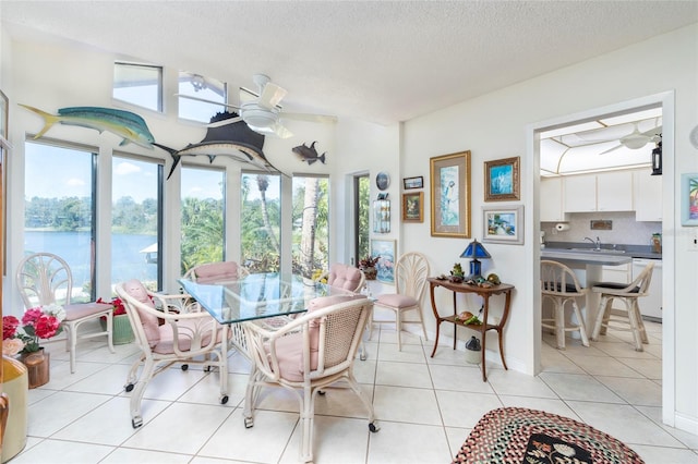 dining space with a water view, a textured ceiling, ceiling fan, light tile patterned floors, and sink