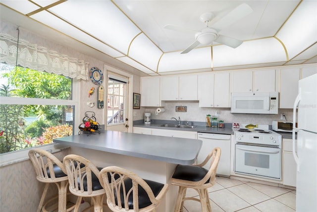 kitchen with white appliances, white cabinetry, sink, and a kitchen breakfast bar