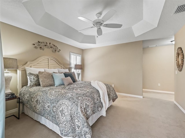 bedroom with light carpet, ceiling fan, a raised ceiling, and a textured ceiling