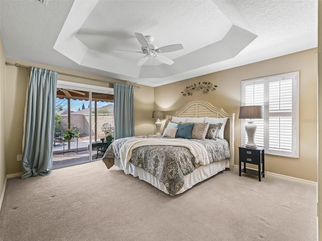 carpeted bedroom with ceiling fan, access to exterior, a raised ceiling, and a textured ceiling