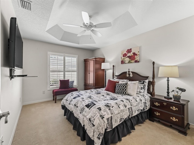 bedroom with ceiling fan, light colored carpet, a textured ceiling, and a tray ceiling