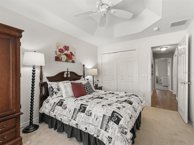 bedroom featuring ceiling fan, a closet, a raised ceiling, and light carpet