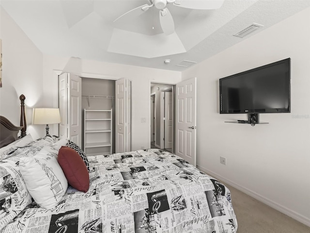 carpeted bedroom featuring ceiling fan, a tray ceiling, and a closet