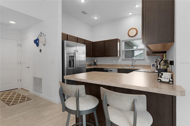 kitchen with kitchen peninsula, sink, a breakfast bar area, light hardwood / wood-style floors, and stainless steel fridge with ice dispenser