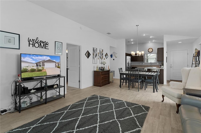 living room with an inviting chandelier, lofted ceiling, sink, and light hardwood / wood-style floors