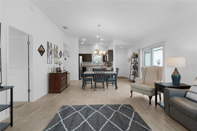 living room with lofted ceiling, a chandelier, and light hardwood / wood-style floors