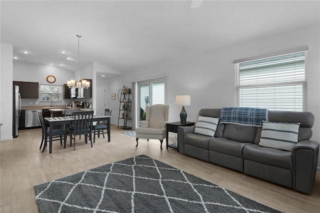 living room featuring an inviting chandelier, lofted ceiling, sink, and light hardwood / wood-style floors