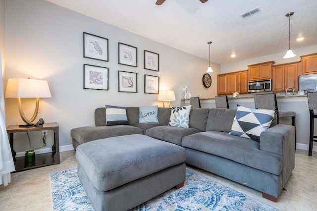 tiled living room with ceiling fan, sink, and a textured ceiling