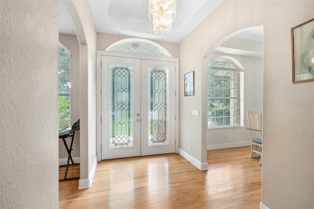 foyer with a raised ceiling, an inviting chandelier, light hardwood / wood-style floors, and french doors