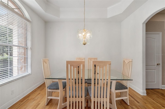 dining space with an inviting chandelier, light hardwood / wood-style floors, and a raised ceiling