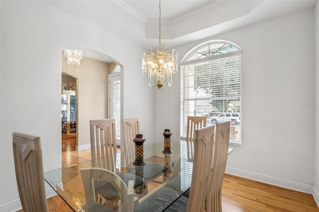 dining space with ornamental molding, a tray ceiling, a chandelier, and light hardwood / wood-style flooring