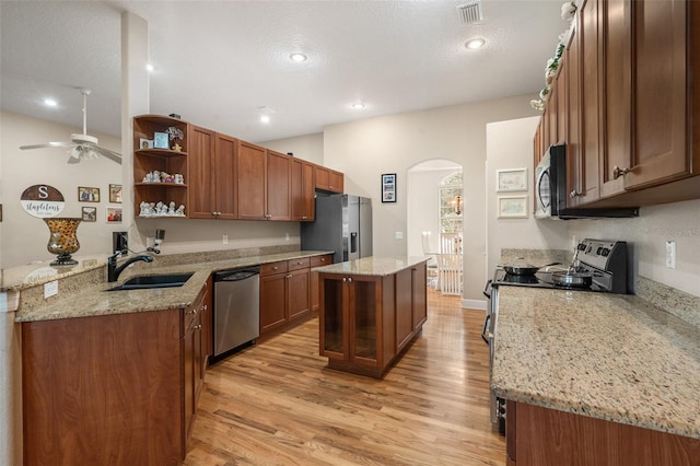 kitchen featuring light wood-type flooring, appliances with stainless steel finishes, kitchen peninsula, a kitchen island, and light stone countertops