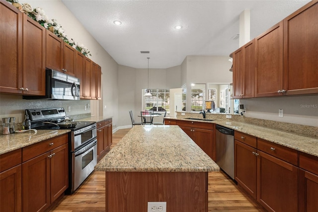 kitchen featuring sink, light hardwood / wood-style flooring, appliances with stainless steel finishes, a kitchen island, and decorative light fixtures