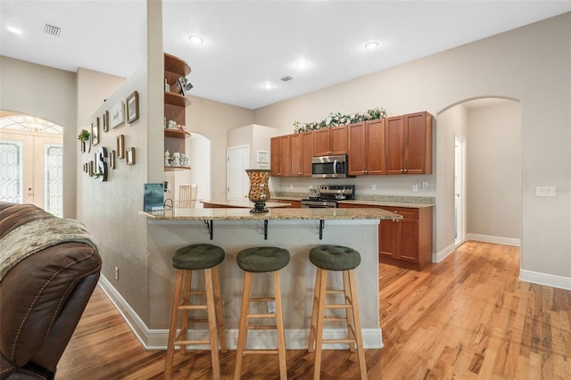 kitchen with a breakfast bar, light stone counters, light wood-type flooring, kitchen peninsula, and stainless steel appliances